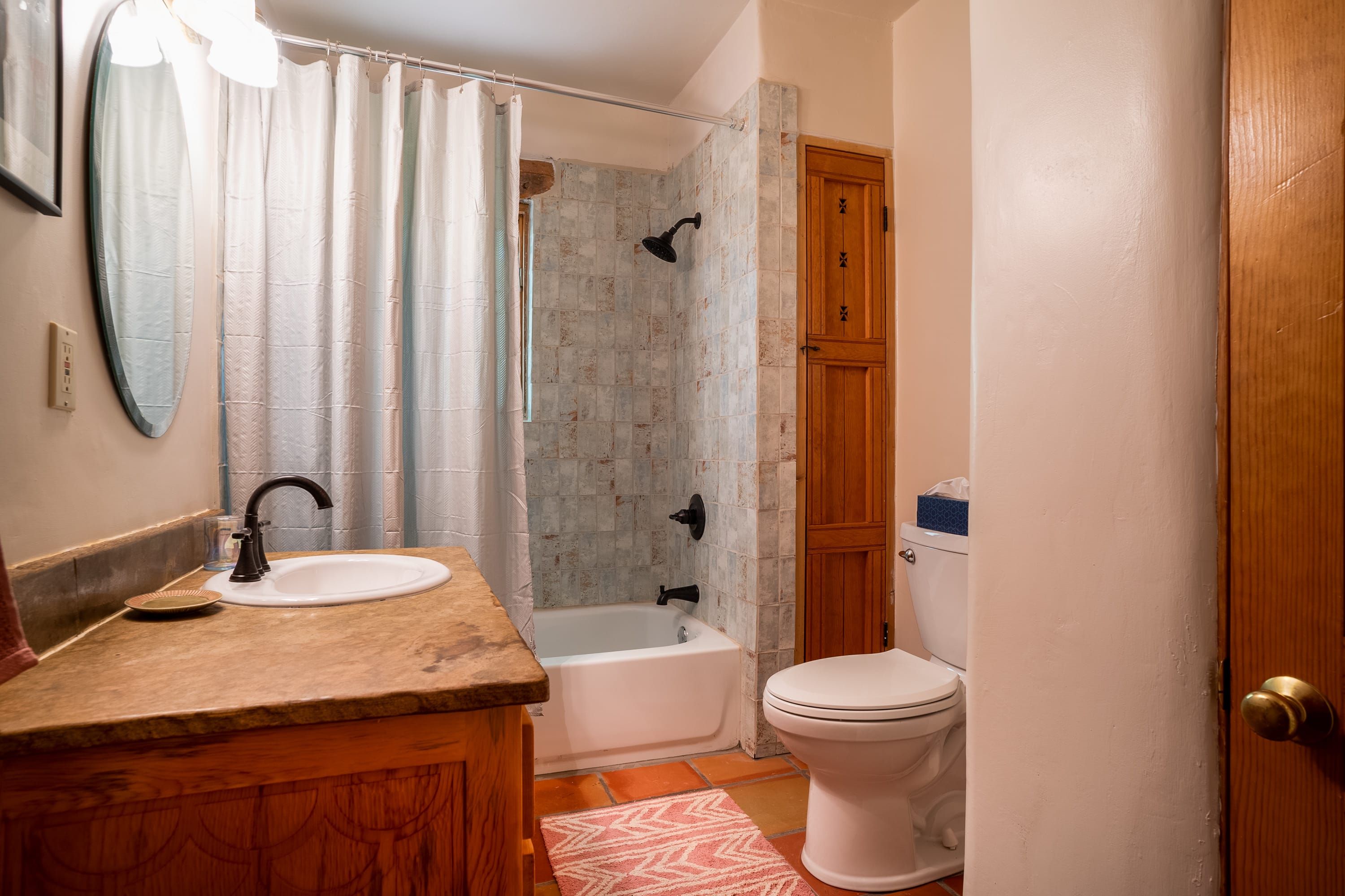 A bathroom with a wooden vanity, a white sink, a shower with a glass door, a toilet, and a wooden door.