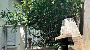 Un patio con una parrilla de ladrillo, una silla azul y un árbol que da sombra.