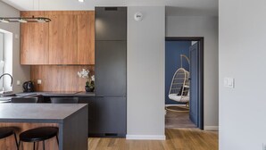 A modern kitchen with wooden cabinets, a stainless steel refrigerator, and a hanging chair in the adjacent room.