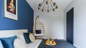 A bedroom with a bed, a hanging chair, a chandelier, and a tray with wine and fruit.