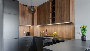 A modern kitchen with wooden cabinets, a black countertop, and a minimalist design. - Spacious apartment on Wróblewskiego (Łódź)