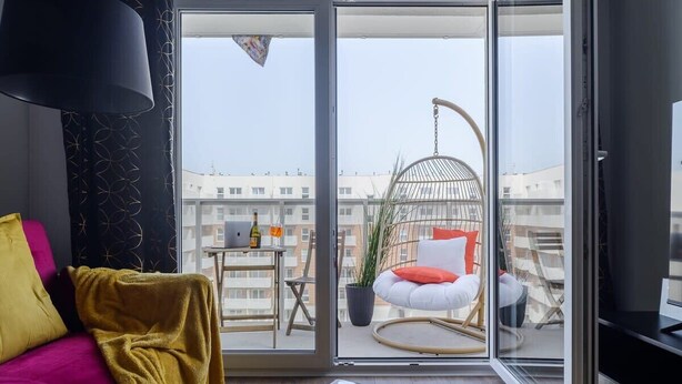 A modern living room with a sofa, a coffee table, and a balcony with a hanging chair and a potted plant. - Spacious apartment on Wróblewskiego (Łódź)