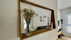A living room with a large mirror, a vase with dried flowers, a sofa, a lamp, and framed pictures on the wall.