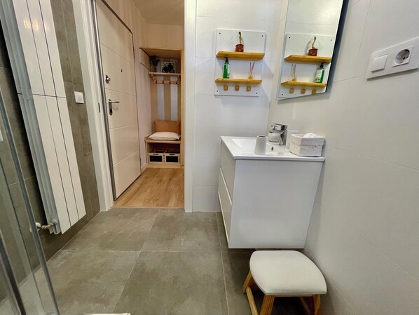 A bathroom with a white sink, a mirror, a small stool, and wooden shelves with toiletries. - El Rincón del Indiano (Santander)
