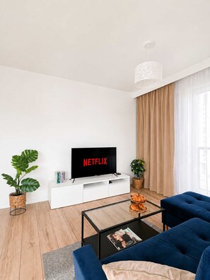 Un salon moderne avec un téléviseur à écran plat, un canapé, une table basse et une plante en pot.