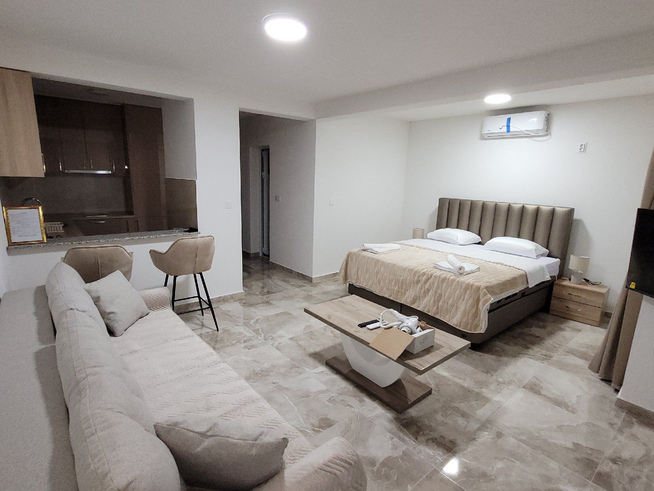 Una habitación de hotel moderna con cama, sofá, mesa de centro, televisor y kitchenette.