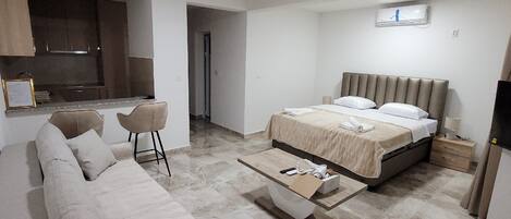 Una habitación de hotel moderna con cama, sofá, mesa de centro, televisor y kitchenette.