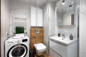 A modern bathroom with a washing machine, toilet, and sink.