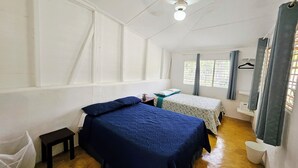 Une chambre avec deux lits, une petite table, une chaise et un ventilateur de plafond.