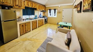 Une cuisine compacte dotée de meubles en bois, d’un réfrigérateur, d’une cuisinière et d’un coin repas comprenant une table et un canapé.