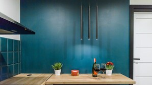 A kitchen with a teal backsplash, a wooden countertop, a bottle of wine, two glasses, and a small potted plant.