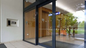 En modern entré till en byggnad med glasdörrar, en kontrollpanel för brandskyddsinspektioner och en skylt som visar riktningen.