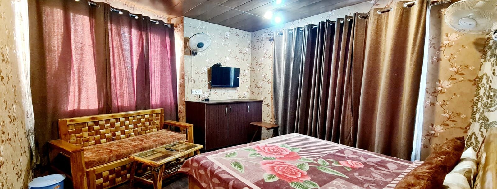 Een slaapkamer met een bed, een houten bankje, een klein tafeltje, een televisie en gordijnen.