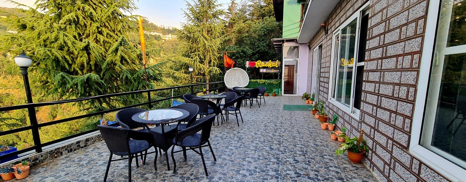 An outdoor patio with round tables and chairs, potted plants, and a view of trees and hills.