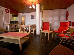 A room with wooden furniture, a red chair, a table with a red tablecloth, and a clock on the wall. - Appartement au cœur de Chamrousse, 50m² avec balcon, pied des pistes, animaux acceptés (Chamrousse)