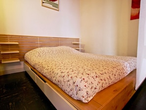 A bed with a floral bedspread, wooden headboard, and a white wall with a small picture. - Appartement au cœur de Chamrousse, 50m² avec balcon, pied des pistes, animaux acceptés (Chamrousse)
