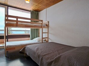 Une chambre avec des lits superposés, donnant sur l’extérieur, avec un plafond en bois et une fenêtre avec des rideaux.