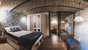 Un dormitorio con cama, mesita de noche y armario. El techo presenta un diseño único, una lámpara colgante y una ventana con persianas.