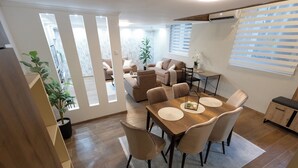 Un comedor con una mesa y sillas de madera, una planta en maceta y vista del salón a través de un separador de vidrio.