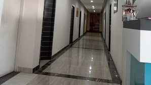 A long, narrow hallway with a marble floor, doors on both sides, and a reception desk on the right. - The Elephant Hotel (Rohtak)