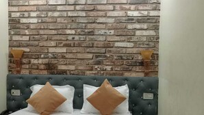 A bedroom with a brick-patterned headboard, a tufted green headboard, and two bedside lamps. - The Elephant Hotel (Rohtak)