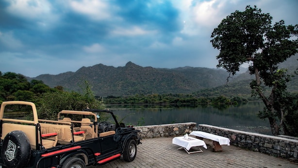 A black convertible car parked on a paved area with a table and chairs set up nearby, overlooking a lake and mountains. - Shivika Lake Hotel Ranakpur (Desuri)