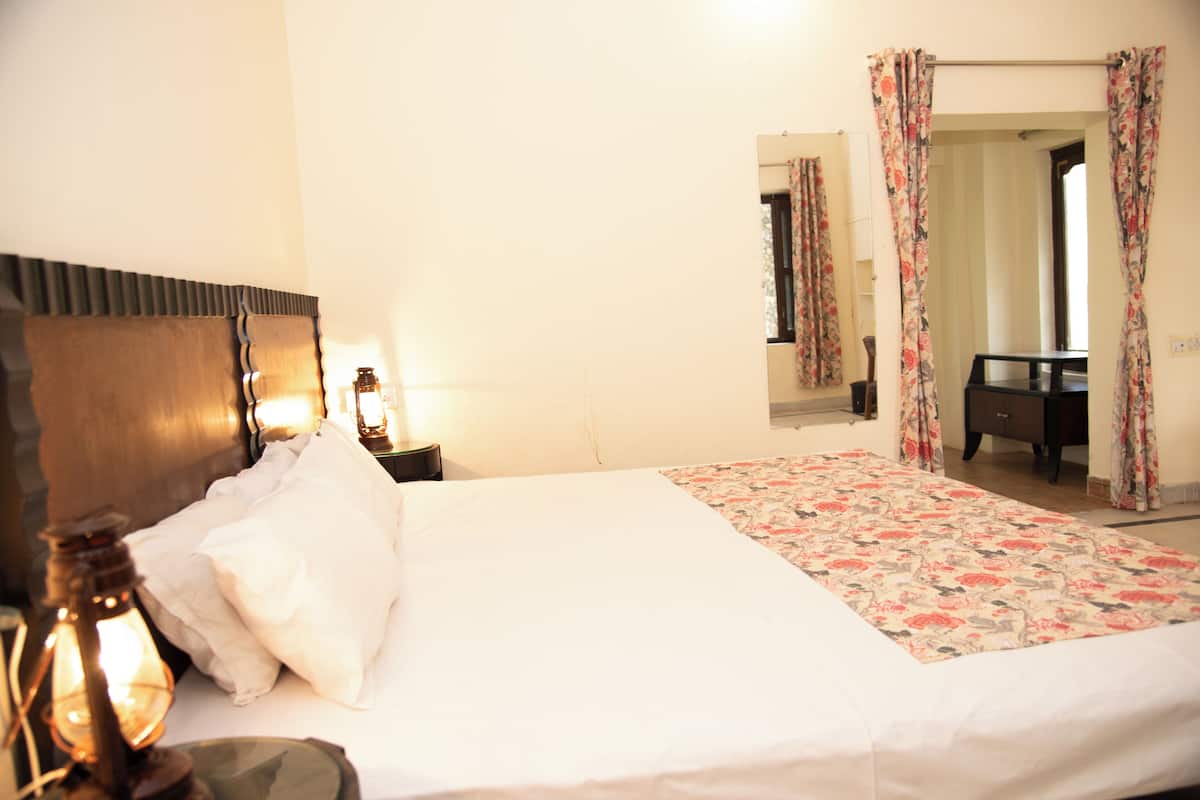 A neatly made bed with white linens, a wooden headboard, and a floral-patterned bedspread. There is a nightstand with a lamp and a mirror on the wall.