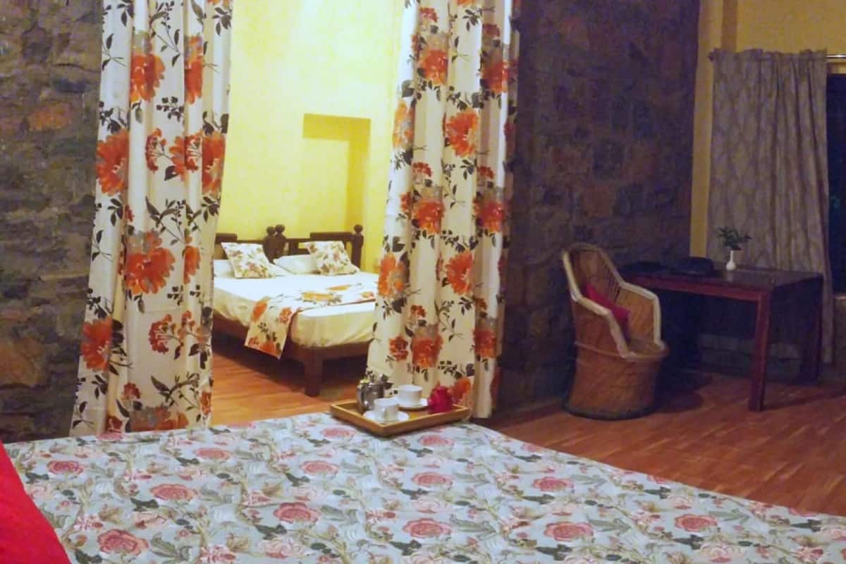 A bedroom with a floral bedspread, a wooden chair, and a small table with a tray of tea items.