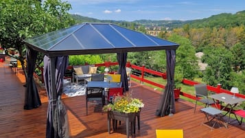 Une terrasse en bois avec des meubles d’extérieur, un espace salon couvert et une vue sur le paysage environnant.