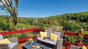 A deck with wicker furniture, a glass table, and a scenic view of a green landscape. - LA BAYARDINE (Sarlat-la-Canéda)