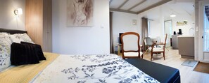 A bedroom with a bed, a bedside table, a chair, a desk, and a bathroom visible through an open door.