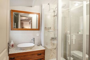 A bathroom with a white sink, a wooden vanity, a glass-enclosed shower, and a mirror above the sink.