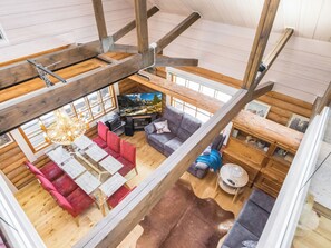Un loft spacieux avec de hauts plafonds, des poutres apparentes, un coin salon confortable avec une cheminée et une vue sur l’extérieur.