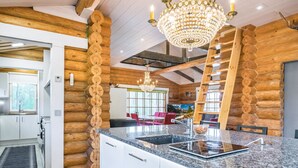 A log cabin interior with a kitchen island, wooden walls, and a chandelier.