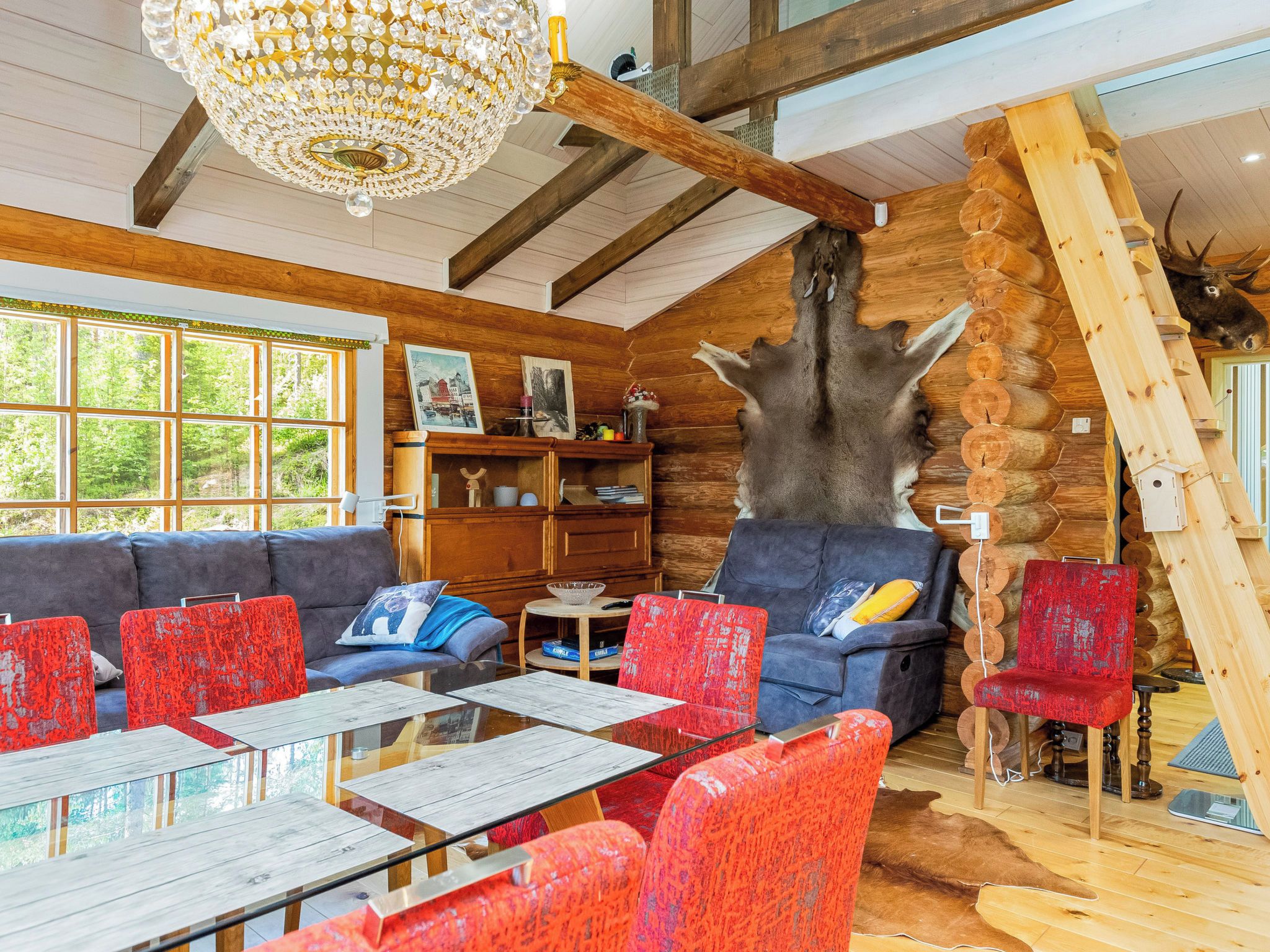 A log cabin interior with a large fireplace, wooden walls, a chandelier, and a dining area.