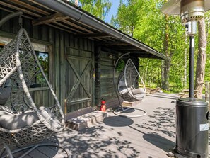 A wooden cabin with a porch, two hanging chairs, a fire extinguisher, and a trash can.