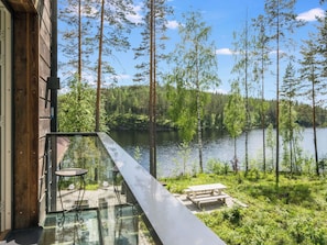 Un balcon doté d’une balustrade en verre, donnant sur un lac, entouré d’arbres et bordé d’un bâtiment en bois.