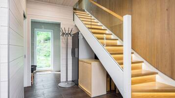 A modern interior with a wooden staircase, a coat rack, and a door leading to a bright outdoor area.