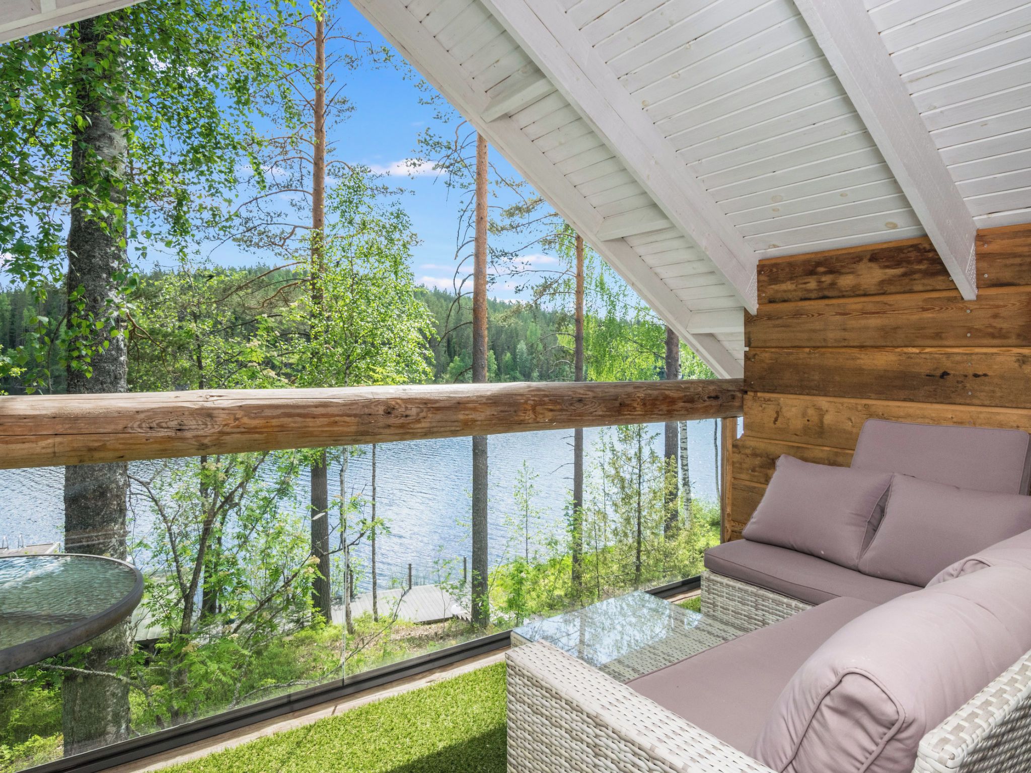 A wooden cabin with a glass balcony overlooking a forest and a lake.