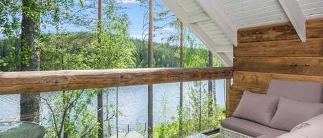 A wooden cabin with a glass balcony overlooking a forest and a lake.