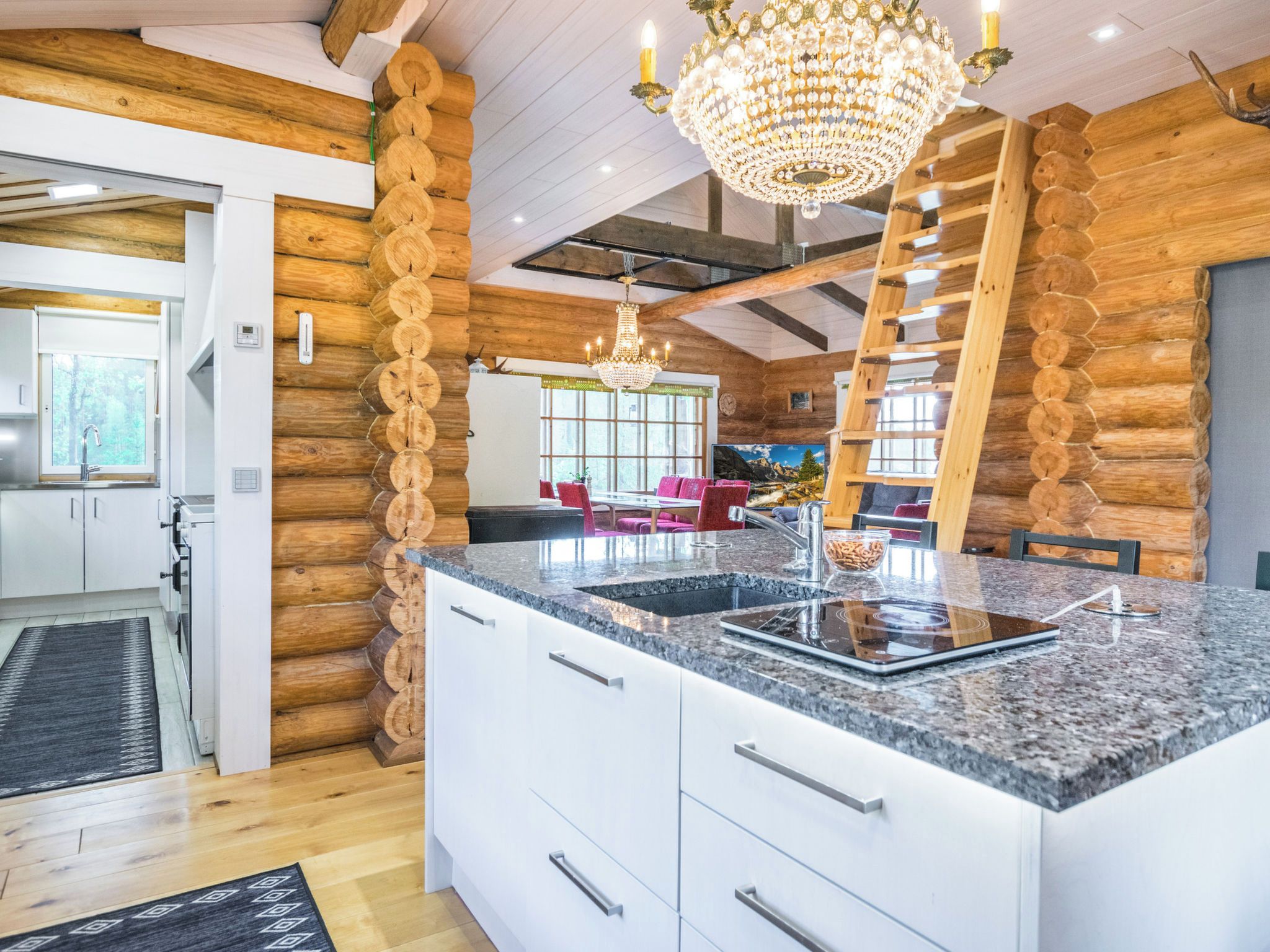 Interior moderno de una cabaña de troncos con una isla de cocina, una araña y un comedor.