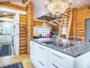 Intérieur moderne d’une cabane en rondins, avec un îlot de cuisine, un lustre et un coin repas.