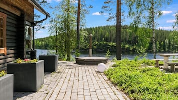 A wooden cabin with a paved patio overlooking a lake, surrounded by trees.