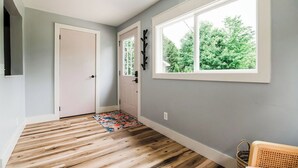 Un pasillo con piso de madera, una puerta blanca y una ventana con vista a árboles.