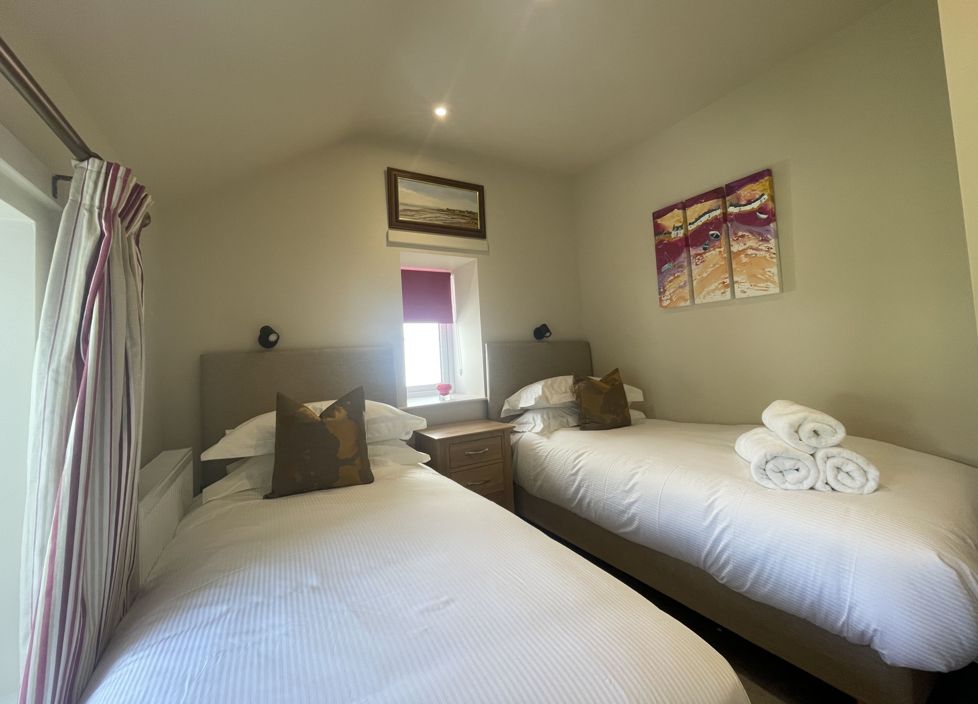 A hotel room with two single beds, a nightstand, a window with a view, and a painting on the wall.