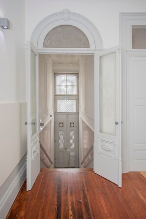 Un pasillo con piso de madera, paredes blancas y una puerta con un ventanal decorativo.