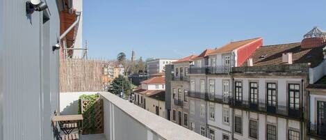A balcony with a wooden table and chairs, overlooking a cityscape with buildings and a clear blue sky.