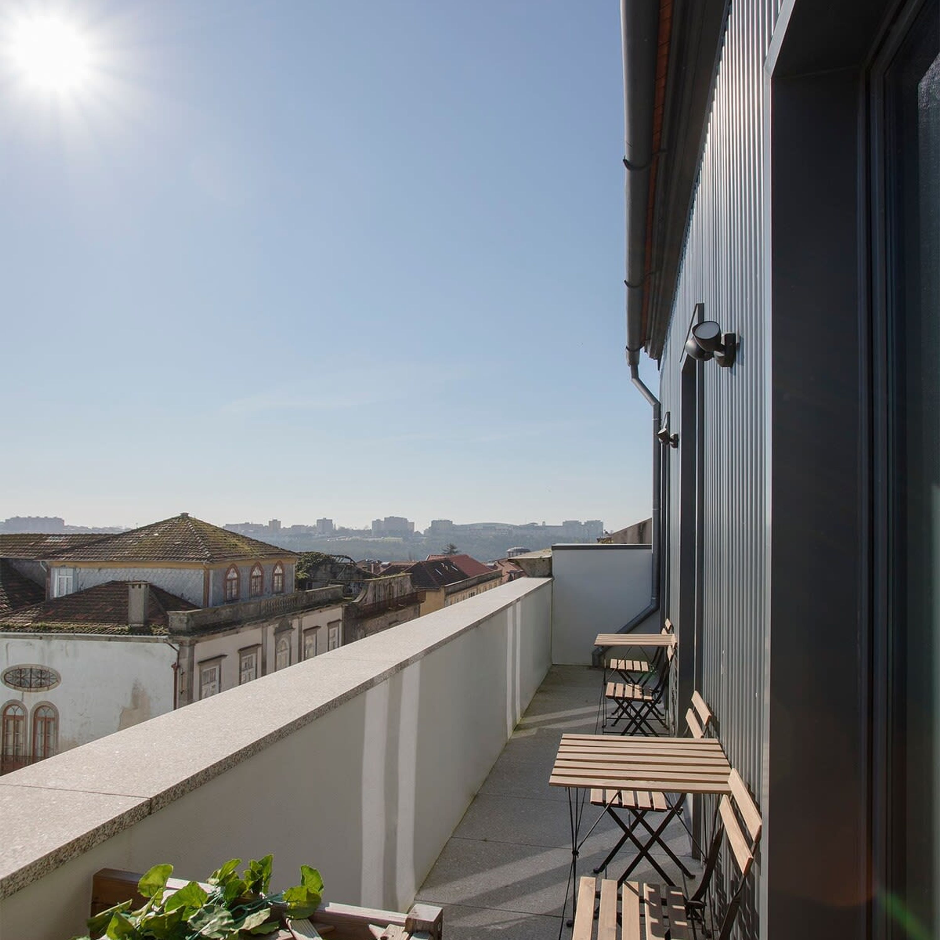 A balcony with a view of a cityscape, a wooden bench, and a potted plant.