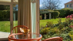 A glass-enclosed patio with wicker furniture, a view of a well-maintained garden, and a building in the background. - Liiiving in Porto Garden Pool House (Porto)