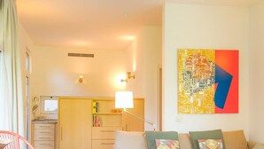 A living room with a sofa, a dining table with chairs, a kitchen in the background, and a colorful abstract painting on the wall. - Liiiving in Porto Garden Pool House (Porto)